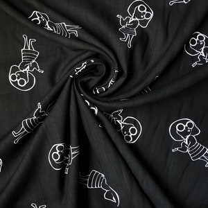 May include: Black fabric with a white repeating pattern of a person wearing glasses and a dress. The fabric is folded in a spiral shape.