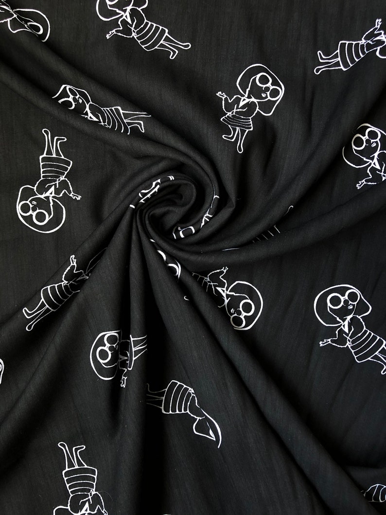 May include: Black fabric with a white repeating pattern of a person wearing glasses and a dress. The fabric is folded in a spiral shape.