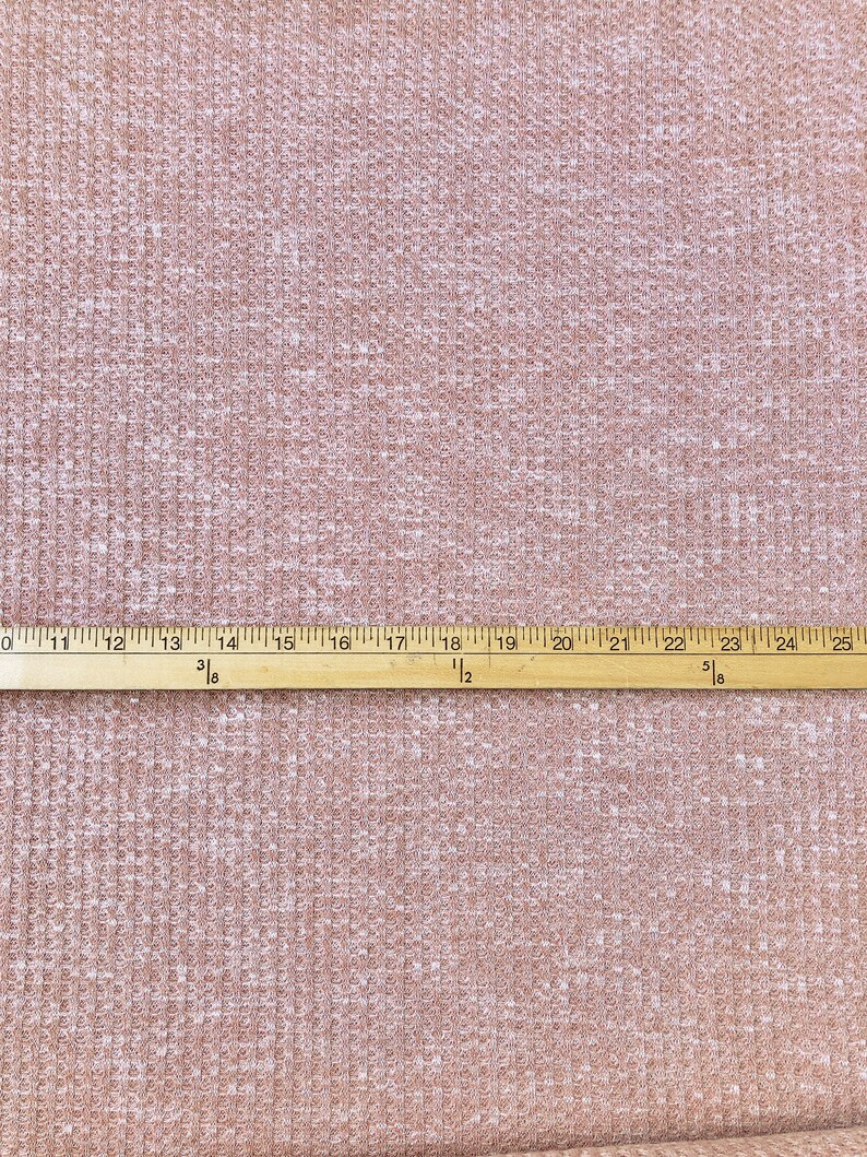 May include: A close-up of a light brown waffle knit fabric with a white ruler measuring 25 inches.