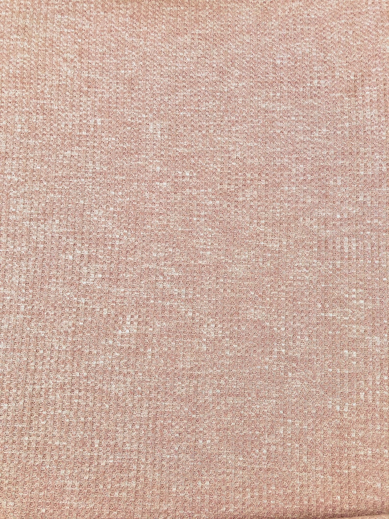 May include: A close-up of a soft, textured fabric in a light pink color. The fabric has a waffle-like texture and a subtle sheen.