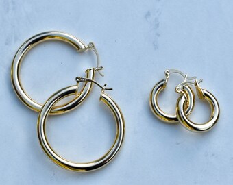 May include: Two pairs of gold hoop earrings. The larger pair is thicker and has a diameter of about 2 inches. The smaller pair is thinner and has a diameter of about 1 inch.