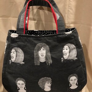 K&ouml;nnte beinhalten: Schwarze Tragetasche mit rotem Besatz an den Griffen. Die Tasche hat ein sich wiederholendes Muster aus schwarz-wei&szlig;en Illustrationen von Frauenportr&auml;ts.