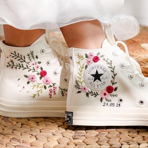 May include: Cream-colored high-top sneakers with floral embroidery. The sneakers feature pink and red flowers with green leaves. The Converse logo is visible on the side. The date "21.09.24" is embroidered on the side of the shoe.