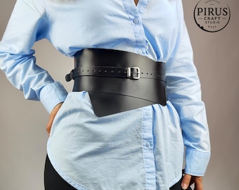 Puede incluir: Un cinturón ancho de cuero negro con hebilla plateada se lleva sobre una camisa azul claro. El cinturón tiene un diseño asimétrico único y se ajusta a la cintura. El logotipo de la tienda Etsy es visible en la esquina superior derecha.