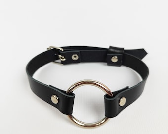 May include: Black leather choker with a silver ring and silver hardware. The choker is handmade and features the text "PIRUS CRAFT STUDIO ETSY" on a circular tag.