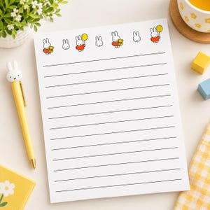 May include: A white lined notepad featuring a repeating pattern of Miffy the rabbit characters at the top, with some holding yellow balloons or teddy bears. The notepad is accompanied by a yellow pen with a Miffy character topper.