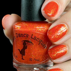 May include: A clear glass bottle of orange nail polish with gold glitter. The bottle is labeled "Rain Dance Lacquer" and "10 Free".
