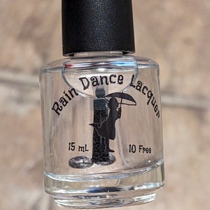 May include: Clear nail polish bottle with a black cap. The bottle has the text "Rain Dance Lacquer" and a silhouette of a person with an umbrella. The bottle contains 15 mL of polish and is labeled "10 Free".