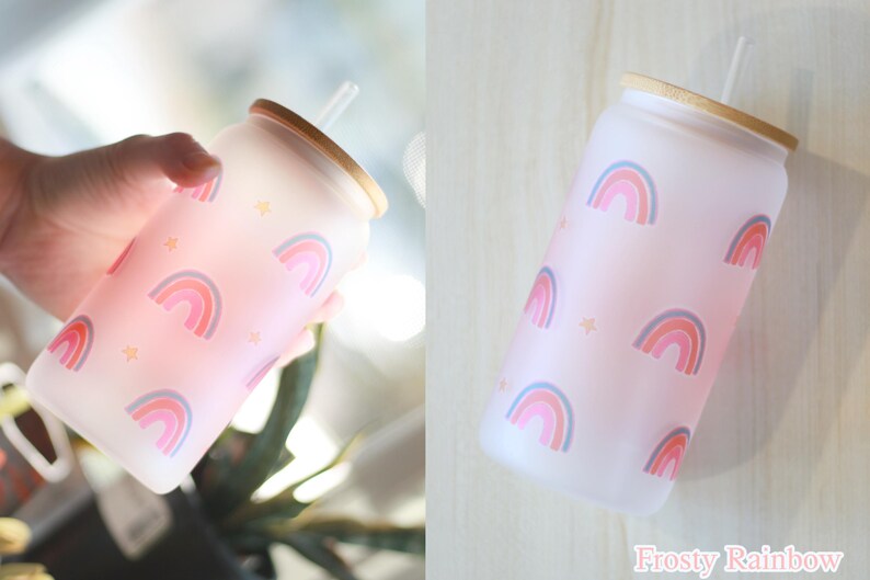 May include: A frosted glass water bottle with a pink and white rainbow pattern and a bamboo lid. The bottle has a straw and the text "Frosty Rainbow" is printed on the bottom.