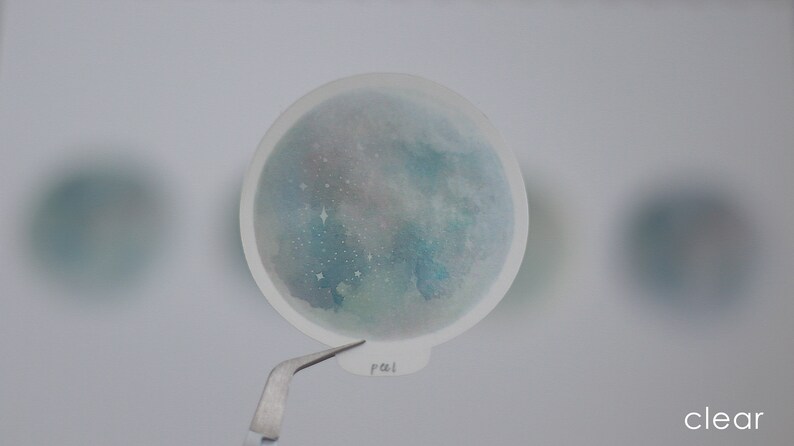 Puede incluir: Una pegatina transparente con un dise&ntilde;o de acuarela de una galaxia azul y verde con estrellas blancas. La pegatina tiene la palabra "pal" escrita en ella.
