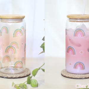 May include: Two glass jars with bamboo lids and rainbow designs. The jar on the left is empty, while the jar on the right is filled with a pink liquid. Both jars are sitting on a woven coaster. The text "Clear Rainbow" is visible at the bottom of the image.