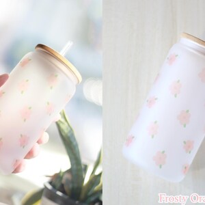 May include: A frosted glass water bottle with a floral pattern and a bamboo lid and straw. The bottle is decorated with a light pink floral pattern.