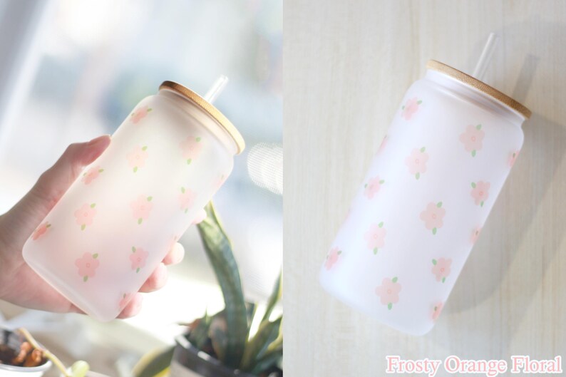 May include: A frosted glass water bottle with a floral pattern and a bamboo lid and straw. The bottle is decorated with a light pink floral pattern.