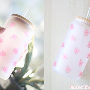May include: A frosted glass water bottle with a pink floral pattern and a bamboo lid. The bottle has a straw.
