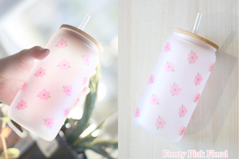 May include: A frosted glass water bottle with a pink floral pattern and a bamboo lid. The bottle has a straw.