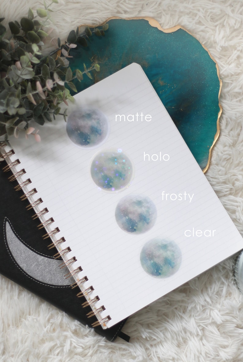 Puede incluir: Cuatro pegatinas en forma de luna con un dise&ntilde;o de galaxia, etiquetadas como "mate", "holo", "escarchado" y "transparente".
