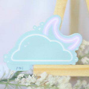 May include: A light blue cloud sticker with a white outline and a pink neon crescent moon. The sticker has a white "peel" label on the bottom.