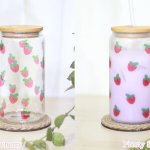 May include: Two glass jars with bamboo lids and strawberrry designs. The jar on the left is clear and the jar on the right is filled with a light purple liquid. Both jars are sitting on a brown rope coaster. The text "Clear Strawberry" is below the left jar and the text "Frosty Strawberry" is below the right jar.