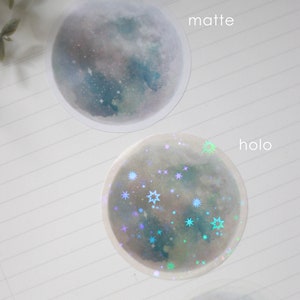 Puede incluir: Dos pegatinas redondas con un dise&ntilde;o de luna de acuarela. La pegatina superior es mate y la pegatina inferior es hologr&aacute;fica con estrellas iridiscentes.