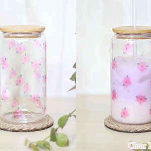 May include: Clear glass jar with a pink floral pattern and a wooden lid. The jar is filled with a light purple liquid and has a straw.