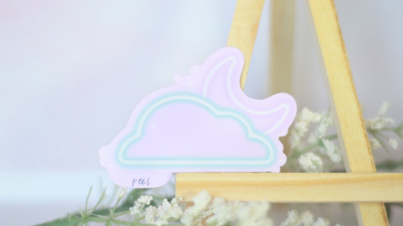 May include: A pastel purple cloud sticker with a crescent moon outline. The sticker has a light blue outline and the word "peel" written on the bottom.