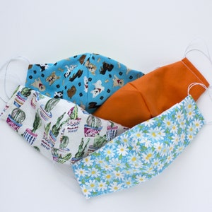 May include: Three fabric face masks with different patterns. One mask is orange, one has a cactus pattern, and one has a blue and white daisy pattern.