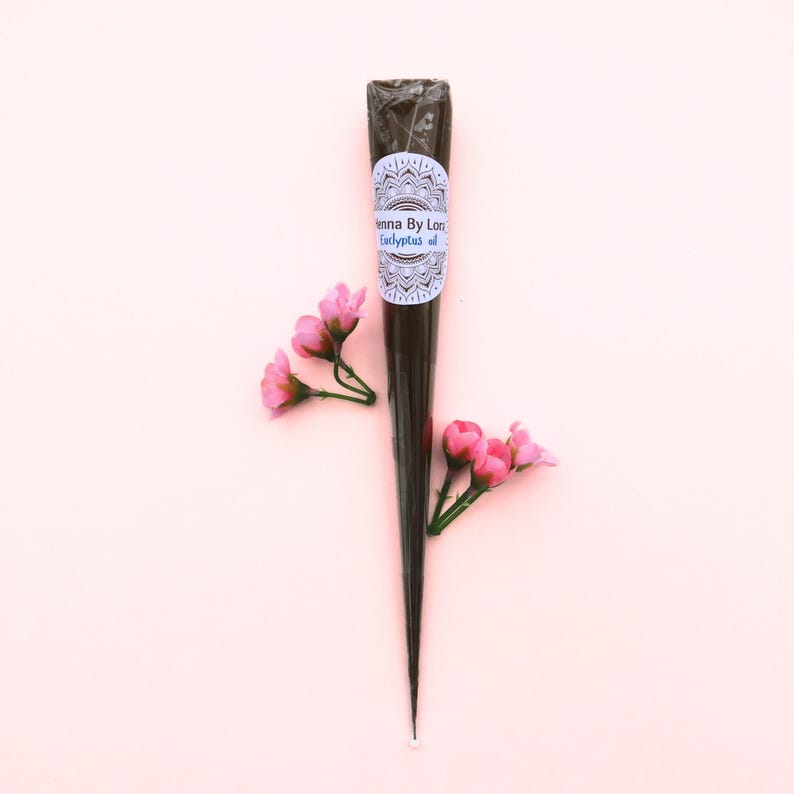 May include: A dark brown henna cone with a white label featuring the text "Henna By Lon Eucalyptus oil". The cone is surrounded by pink flowers on a light pink background. The henna cone is a traditional body art product.