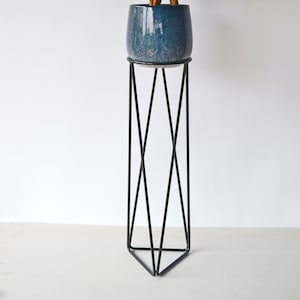 May include: A dark blue ceramic planter with a green leafy plant on a black metal plant stand with a triangular base.