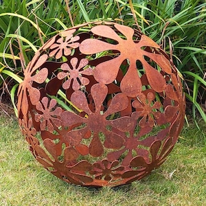 May include: A large, rusty metal sphere with a decorative design of cut-out flowers. The sphere is sitting on a bed of green grass.