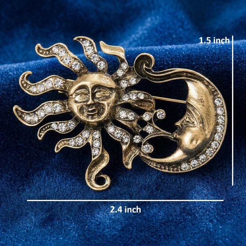 May include: A gold-toned brooch featuring a sun and moon design. The sun has a smiling face and radiating rays, and the moon has a face. Both are adorned with clear rhinestones. The brooch measures 2.4 inches wide and 1.5 inches high.