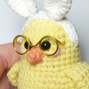 May include: A crocheted yellow chick wearing white bunny ears and gold-rimmed glasses.