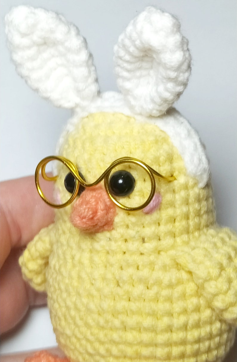 May include: A crocheted yellow chick wearing white bunny ears and gold-rimmed glasses.