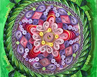 May include: A colorful paper quilling mandala with a green background. The mandala is made up of many small, rolled paper pieces in shades of pink, purple, red, and yellow. The center of the mandala is a spiral of yellow paper.