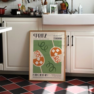 Pode incluir: Um p&ocirc;ster emoldurado com fundo verde e formas abstratas laranja e brancas. O p&ocirc;ster tem o texto "SPRITZ Delicious! Something Nice 1998" e "Made in Italy Matteo Schilizzi 17 16163 Milano".