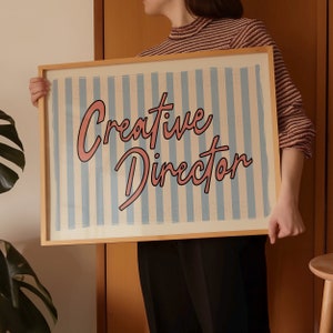 May include: A wooden framed print with blue and white stripes and the text "Creative Director" in pink lettering.