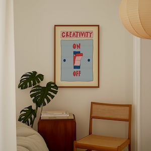 May include: A framed art print with a light blue background and the words "CREATIVITY" and "ON OFF". The artwork depicts a light switch with red and pink accents. The print is in a brown frame and hangs on a white wall.