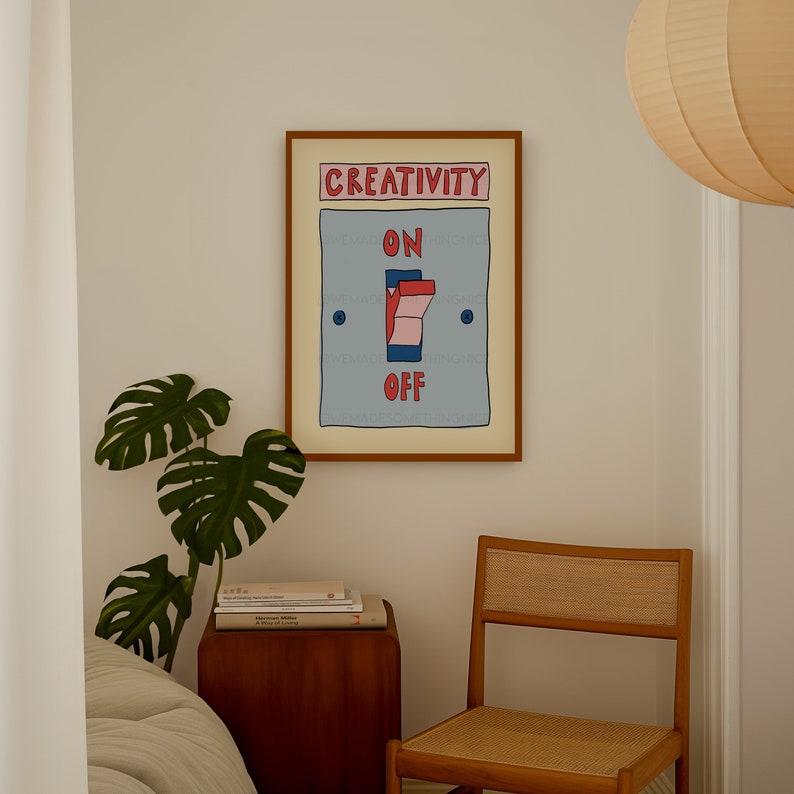 May include: A framed art print with a light blue background and the words "CREATIVITY" and "ON OFF". The artwork depicts a light switch with red and pink accents. The print is in a brown frame and hangs on a white wall.