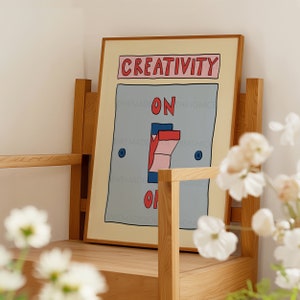 May include: A framed art print featuring a whimsical illustration of a light switch. The word "CREATIVITY" is above the switch, with "ON" and "OFF" on either side. The switch is in the "ON" position. The artwork is in a wooden frame.