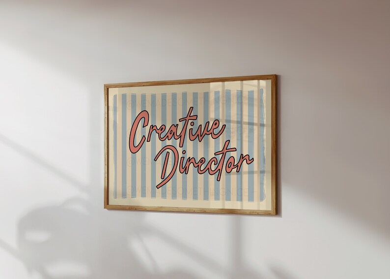 May include: A framed print with a blue and white striped background and the text "Creative Director" in pink cursive lettering.