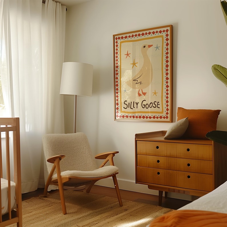 Puede incluir: Una silla de guarder&iacute;a blanca con un coj&iacute;n blanco esponjoso se encuentra frente a una c&oacute;moda de madera con tres cajones. Una impresi&oacute;n enmarcada de un ganso de dibujos animados con el texto "Silly Goose" cuelga en la pared sobre la c&oacute;moda.