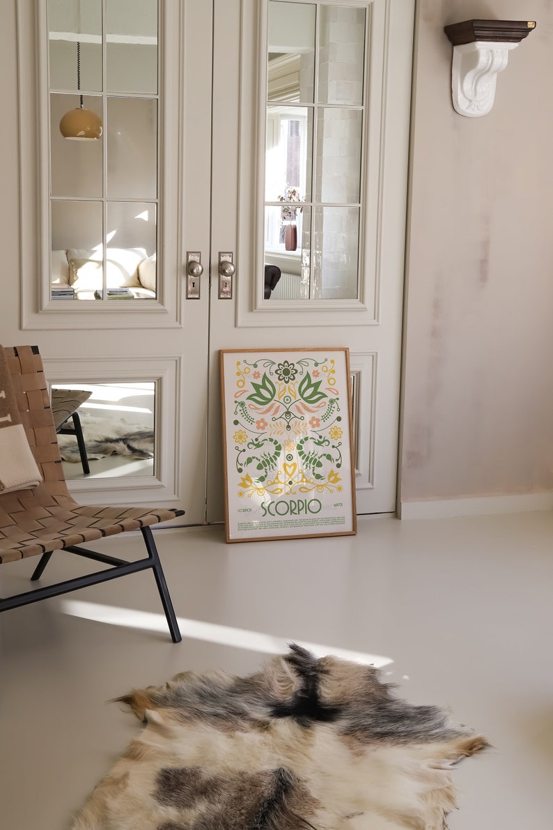 May include: A framed poster with a floral design and the word "SCORPIO" in yellow letters. The poster is on a white floor in a room with white walls and a wooden chair.