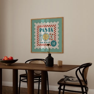 May include: A framed print with a retro pasta stamp design. The artwork displays the word "PASTA", a plate of food, and the text "MADE IN ITALY". The frame is wood-toned, and the background is a light teal colour.