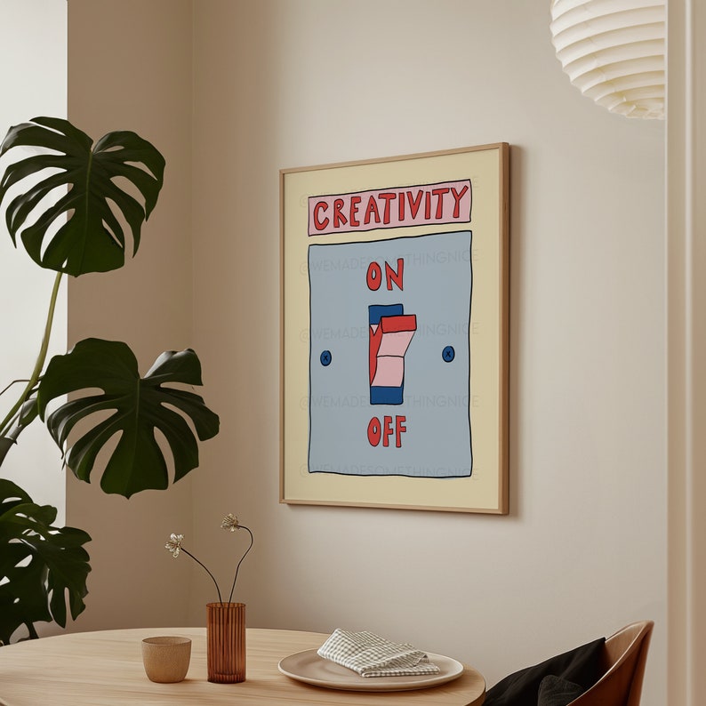 May include: A framed art print featuring a light blue switch with the words "ON" and "OFF". The top of the print reads "CREATIVITY" in red. The switch is in the "ON" position, with a pink and red toggle. The print is in a light wood frame.