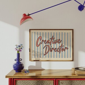 May include: A wooden framed print with a blue and white striped background and the text "Creative Director" in pink lettering.