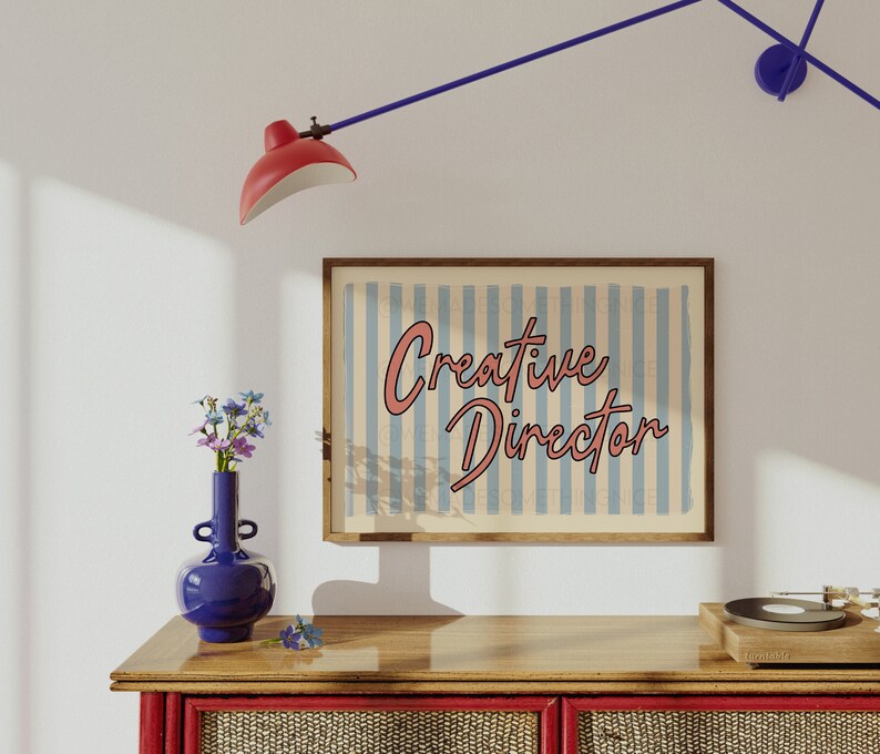 May include: A wooden framed print with a blue and white striped background and the text "Creative Director" in pink lettering.
