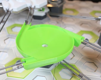 May include: A green plastic track piece for a marble run game. The track piece is a circular ramp with a hole in the center. The track piece is attached to a metal frame.