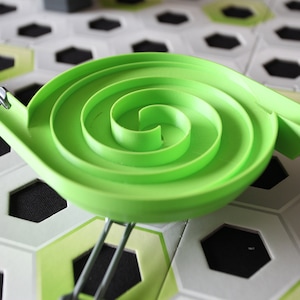 Peut inclure: Une pièce de piste en spirale en plastique vert pour un jeu de course de billes. La piste est fixée à un cadre métallique et est conçue pour envoyer les billes en mouvement circulaire.