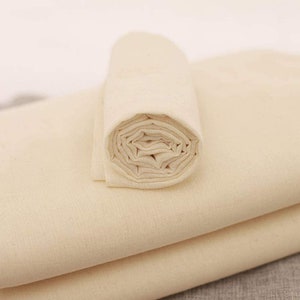 May include: A roll of natural unbleached cotton muslin fabric. The fabric is folded and rolled up, showing the soft, natural texture.