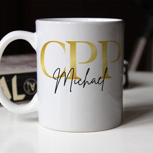 Peut inclure: Une tasse en céramique blanche avec un "CPP" doré et le texte "Michael" en cursive noire sur le devant.