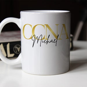 May include: White ceramic mug with the gold text "CCNA" and the name "Michael" in a script font. The mug has a curved handle and is sitting on a white surface.
